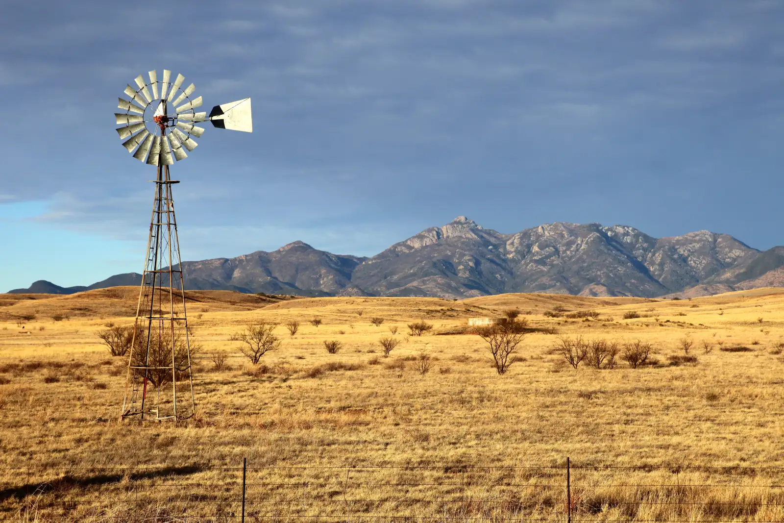 Old windmill on golden grassland near Sonoita, Arizona, with the Santa Rita Mountains under a stormy blue sky.