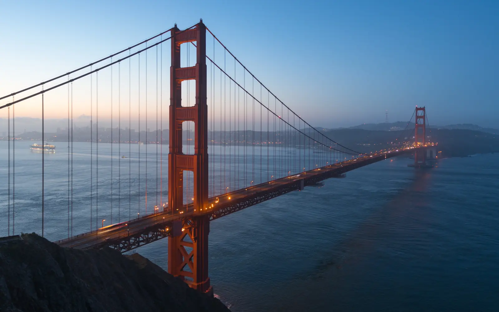 The red Golden Gate Bridge at blue hour from the Marin Headlands, with the San Francisco shoreline across the water.