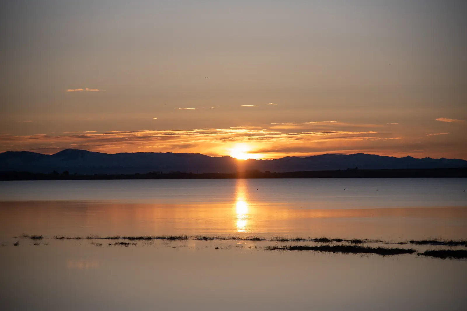Sunrise over Lake Lowell in western Idaho, with the sun rising behind a dark ridge and a golden reflection on calm water.