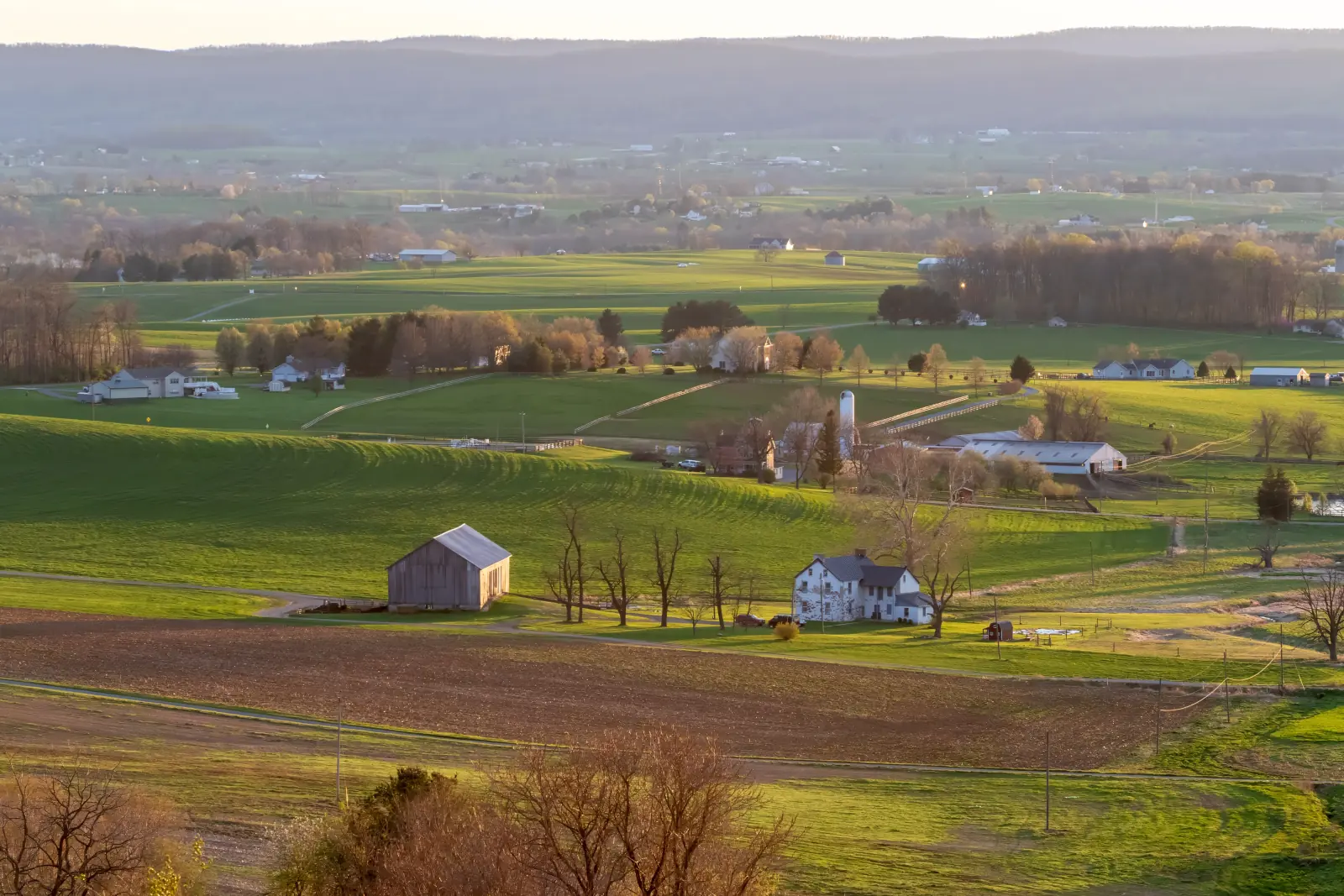 Evening light over green farmland and a historic farmstead in the Middletown Valley of Frederick County, Maryland, with ridges of South Mountain beyond.