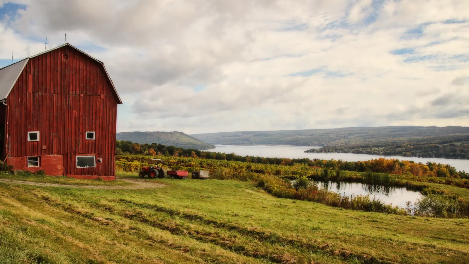 Red barn on a hillside above vineyards in autumn color, looking out over Keuka Lake and the hills beyond.