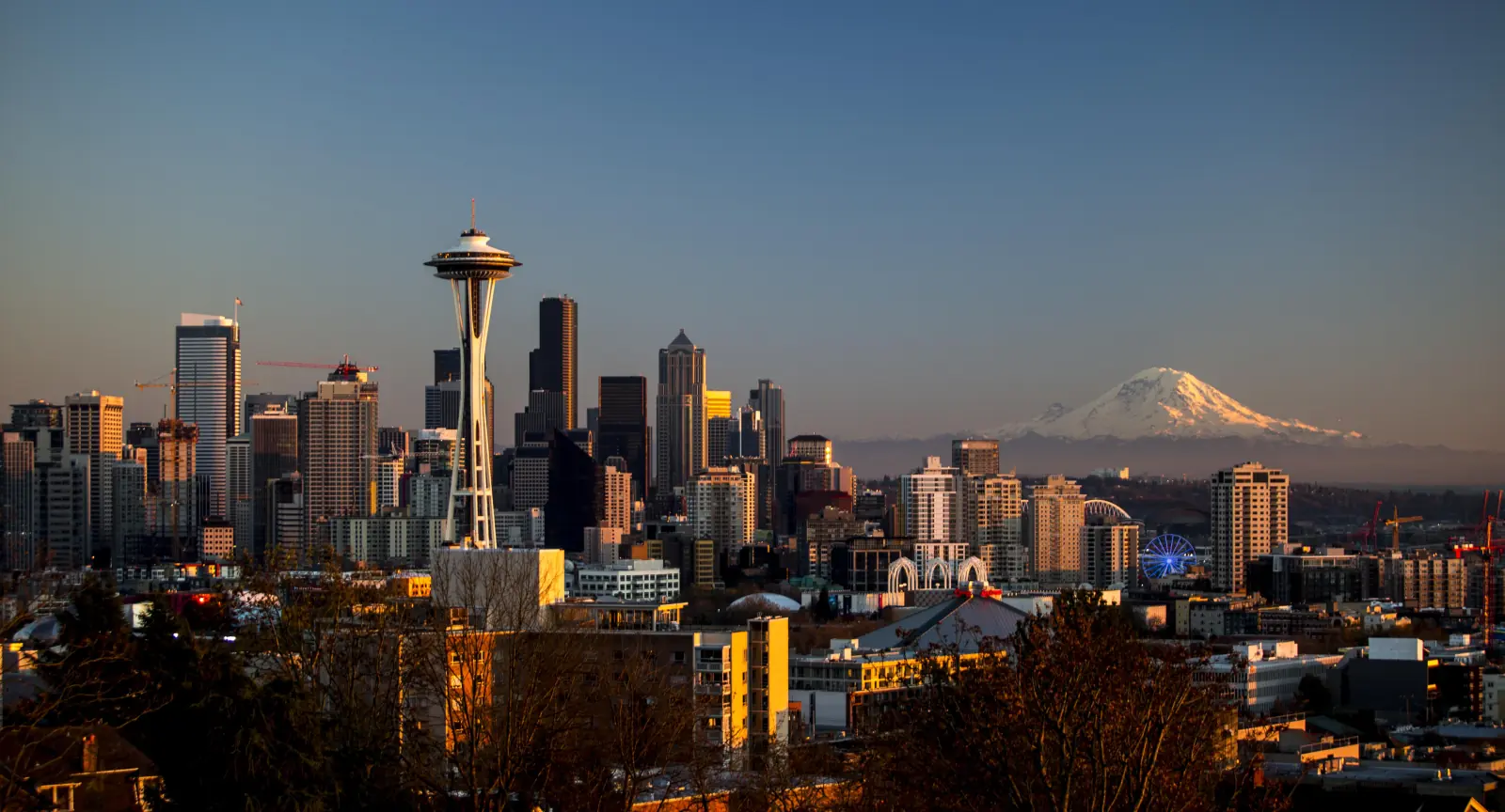 Seattle skyline at sunset from Kerry Park, with the Space Needle and downtown towers in warm light and Mount Rainier glowing on the horizon.
